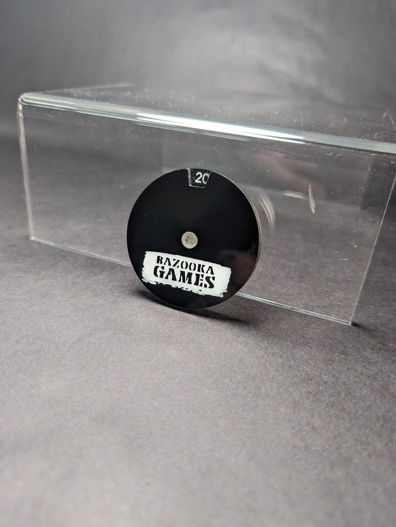 The Bazooka Games Life Counter is a black acrylic piece with "BAZOOKA GAMES" and 20 at the top, upright on a clear stand.