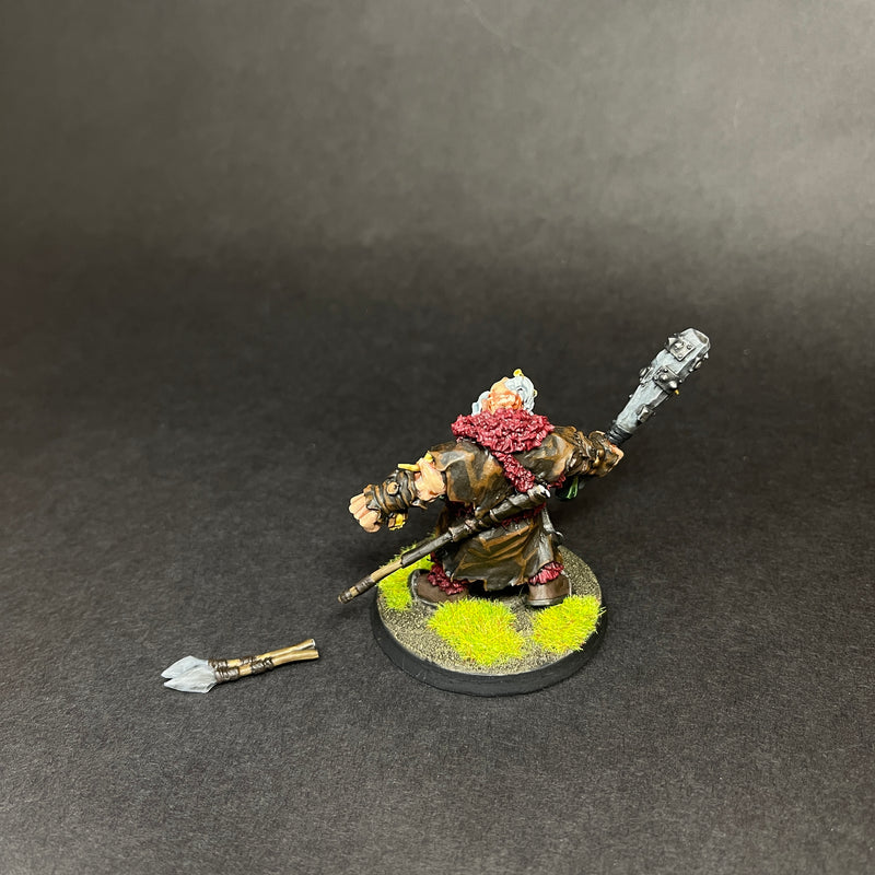 A used Warhammer Age Of Sigmar: Ogor Mawtribes- Icebrow Hunter (L2) stands painted with a fur cloak and large mace on a grassy base, with a broken spear resting nearby against a dark background.