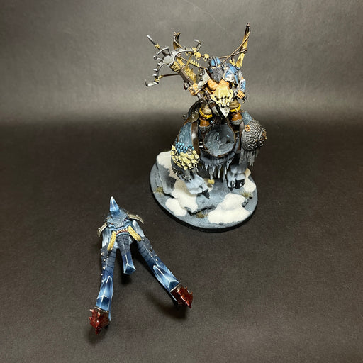 A used Warhammer Age of Sigmar: Ogor Mawtribes - Huskard on Thundertusk miniature, painted and displayed on a snowy base, stands next to a separate blue-armored, legless figure lying on the black background.
