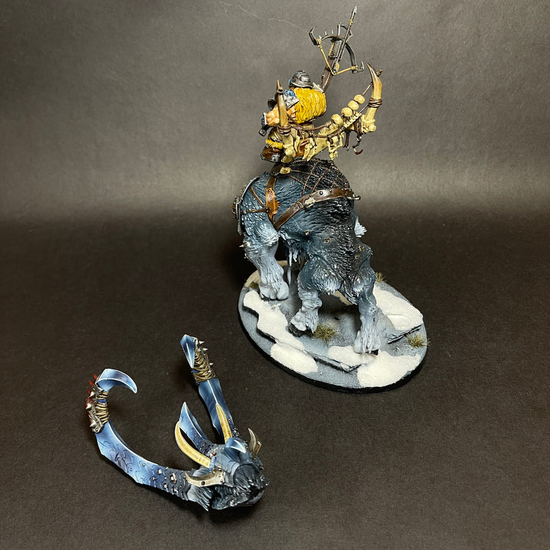 A used Warhammer Age of Sigmar: Ogor Mawtribes - Huskard on Thundertusk miniature is displayed, showcasing a fantasy beast with a rider wielding a bow. The model includes an additional detached horned headpiece placed on the snow-textured base, all presented against a plain dark background.