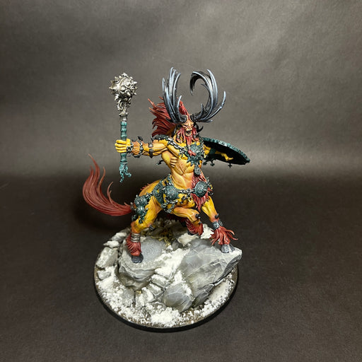 A used Warhammer Age of Sigmar: Destruction – Kragnos, the End of Empires miniature is shown painted with yellow skin, a muscular build, a red mane, and large black horns, wielding a mace and shield while standing atop a snowy rock base.