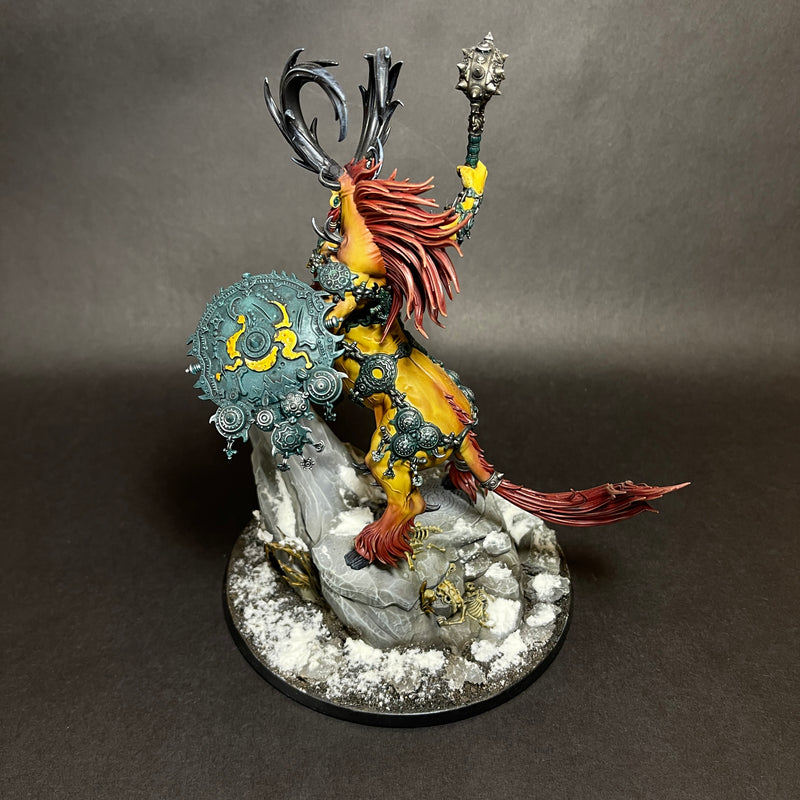 A painted Used Warhammer Age of Sigmar: Destruction - Kragnos, the End of Empires miniature, depicting a beast-like warrior with a red mane, horns, ornate armor, shield, and mace, stands on a snowy rock base against a black background.