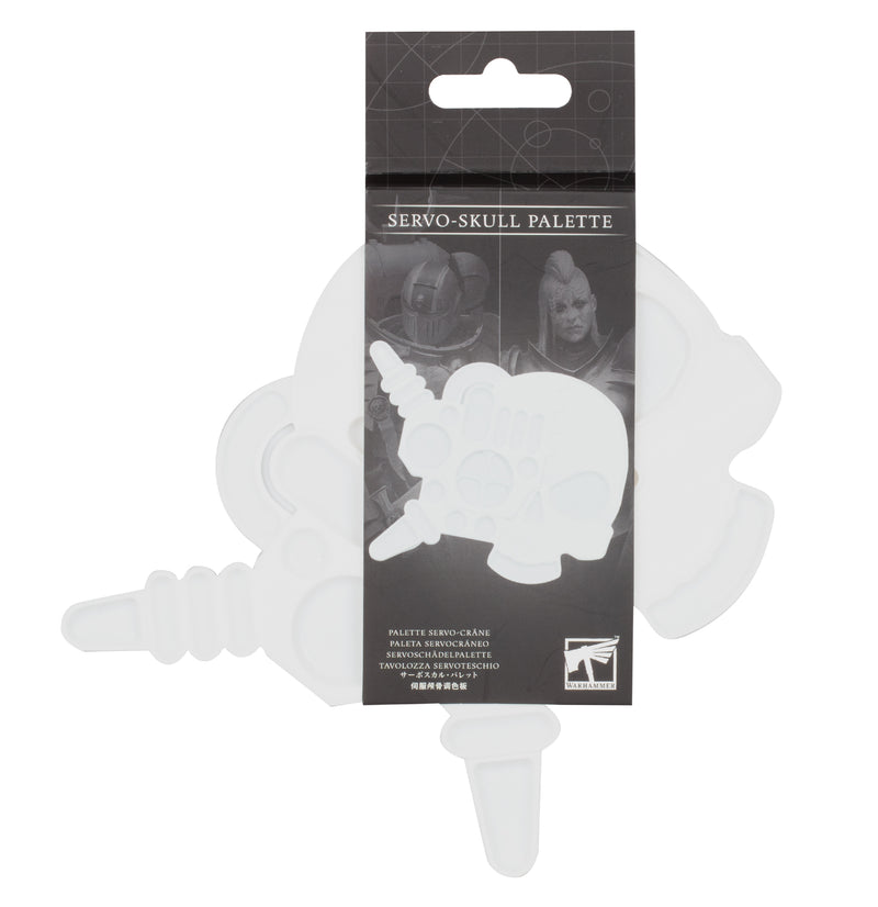 The Warhammer Servo-Skull Palette is a plastic paint palette shaped like a mechanical skull with silicone wells and a plug, packaged in a clear sleeve with sci-fi artwork and multilingual text.