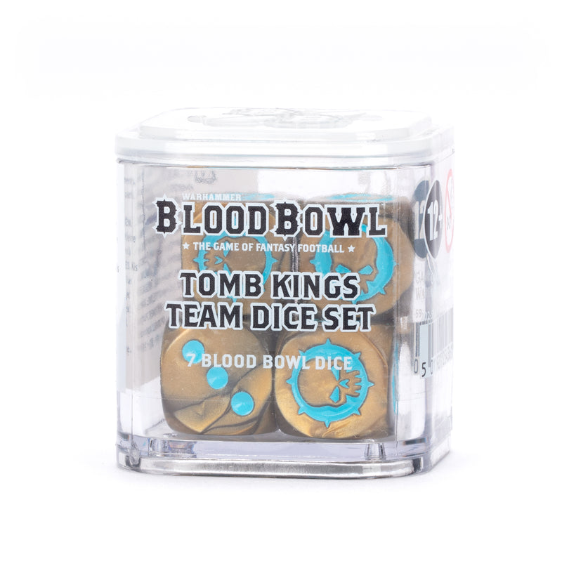 A clear plastic box holds the Blood Bowl: Tomb Kings Team Dice Set from Games Workshop, featuring gold and turquoise dice with unique symbols for the fantasy football game.